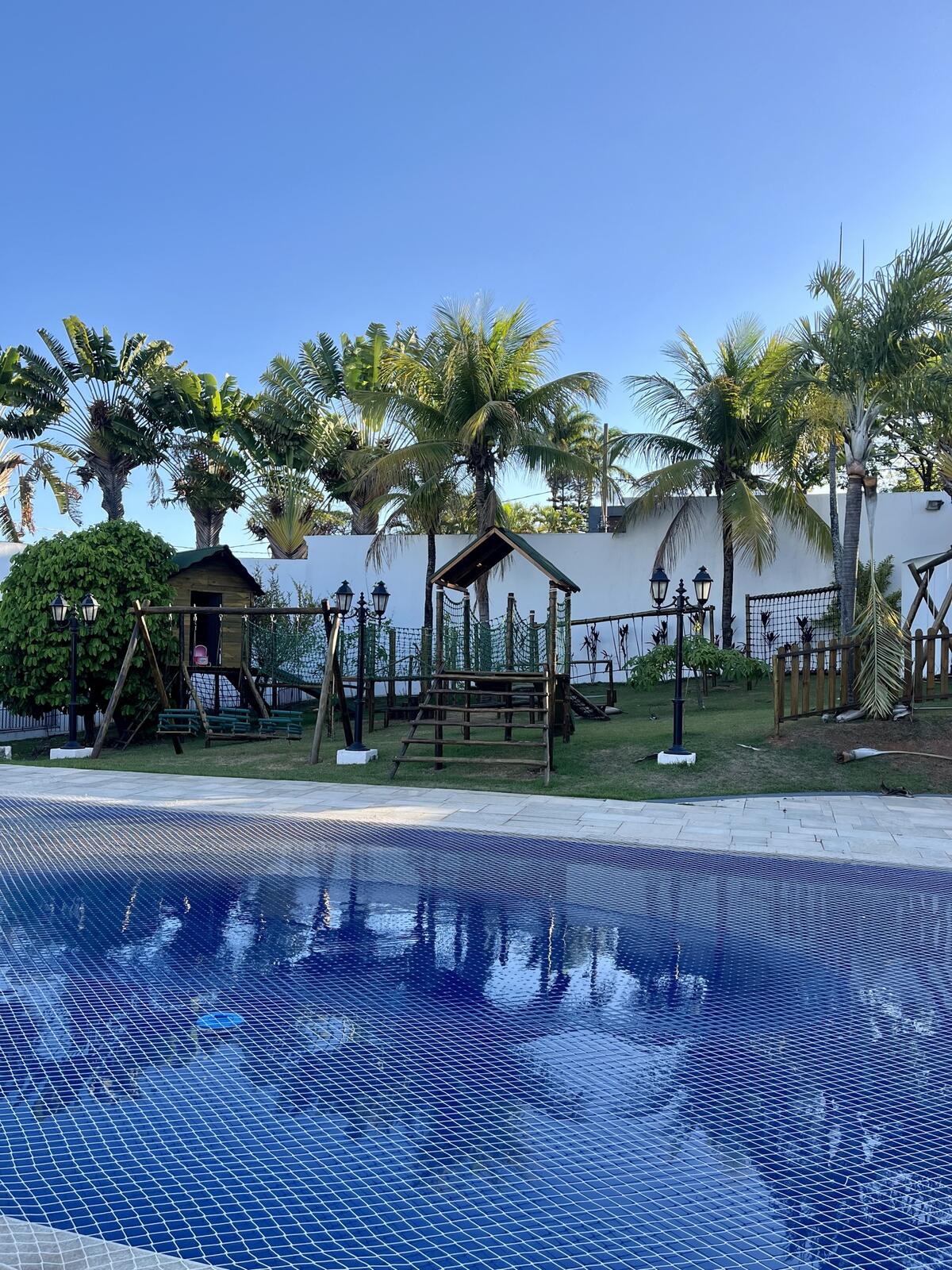 Piscina do Espaço Martinica cercada de coqueiros e o playground ao fundo
